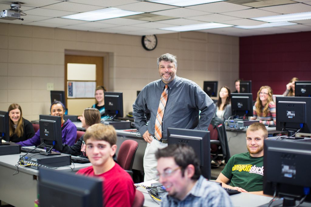 Information Systems Degree Professor and students in computer lab smiling