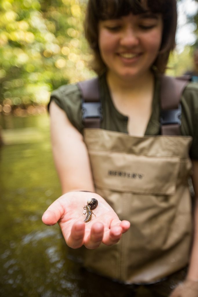 A student in a stream holding a shell and a bug