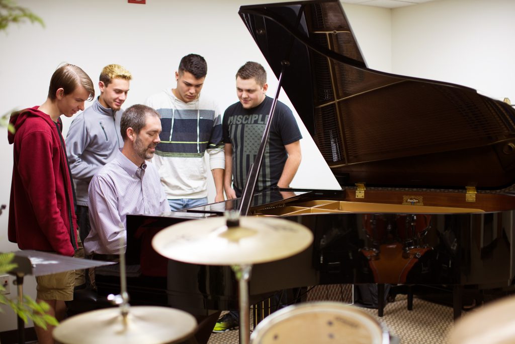 Professor playing the piano with students watching