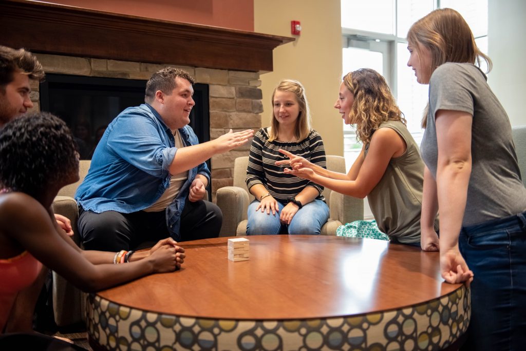 Students at Grace College laugh and engage in a playful group activity around a table, building relationships and exploring ministry opportunities through community.