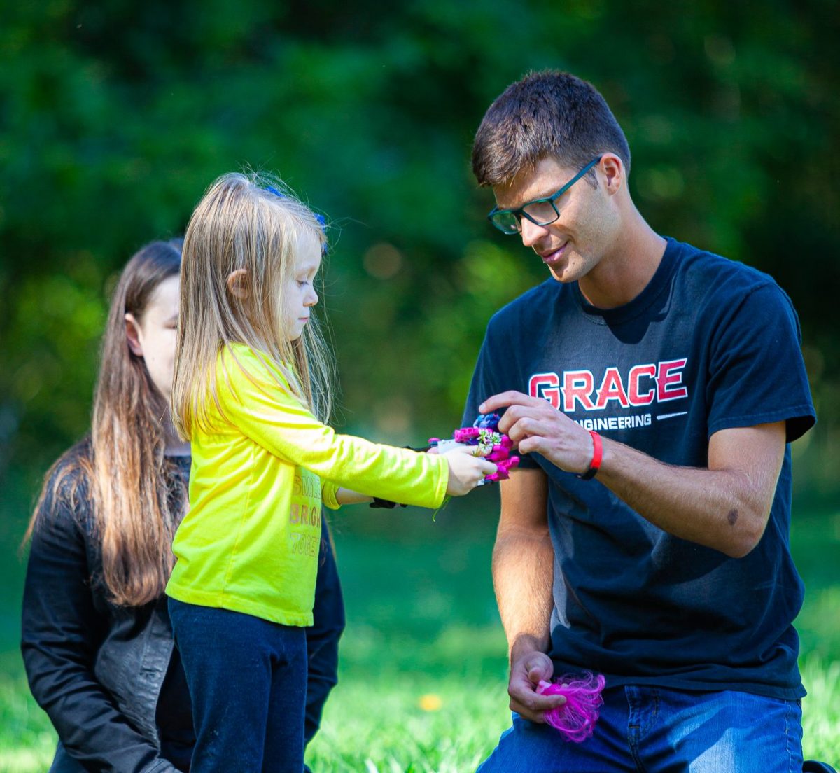 Christian college student wearing a 'Grace Engineering' shirt helps a young girl during a service activity, demonstrating servant leadership and mentorship as core values of what it means to be a Christian college.