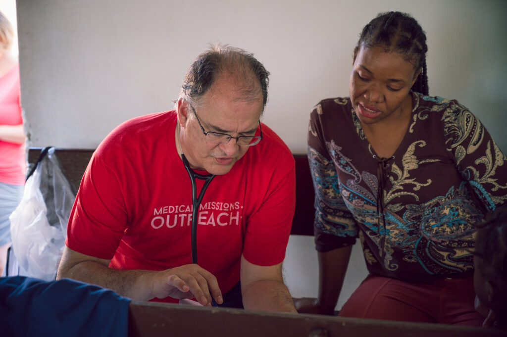 Medical missions worker in a red shirt reviews documents with a local woman in a village clinic, exemplifying cross-cultural care and community engagement inspired by a Christian worldview.