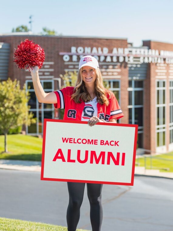 Grace College student with welcome sign for Grace College Alumni