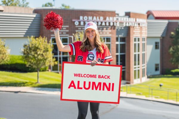 Grace College student with welcome sign for Grace College Alumni