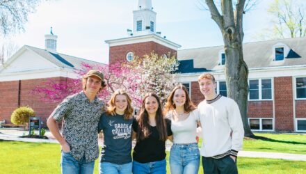 Smiling students standing together on the green lawn in front of a McClain at Grace College a Christian college campus, representing community and faith-based education.