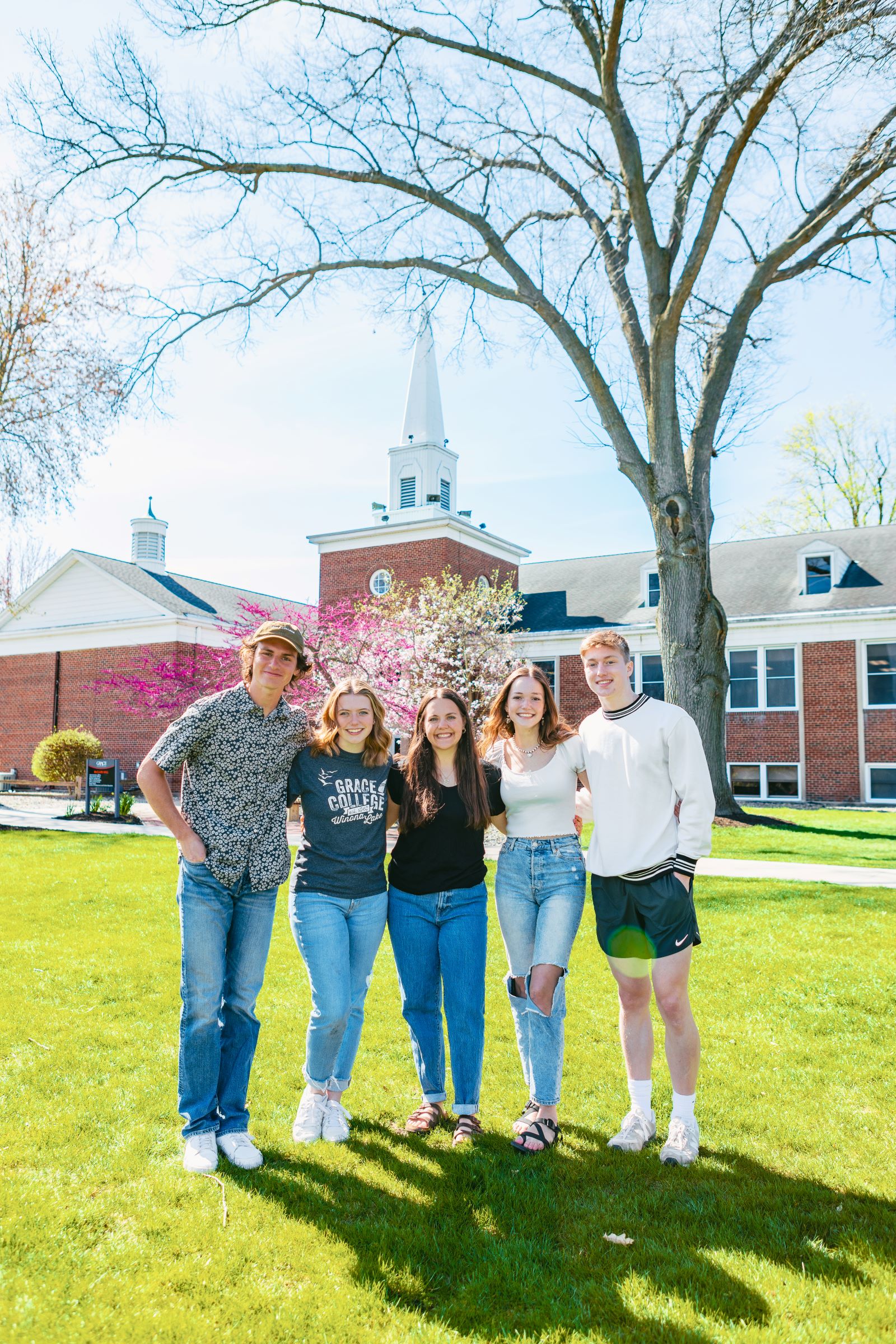 Smiling students standing together on the green lawn in front of a McClain at Grace College a Christian college campus, representing community and faith-based education.